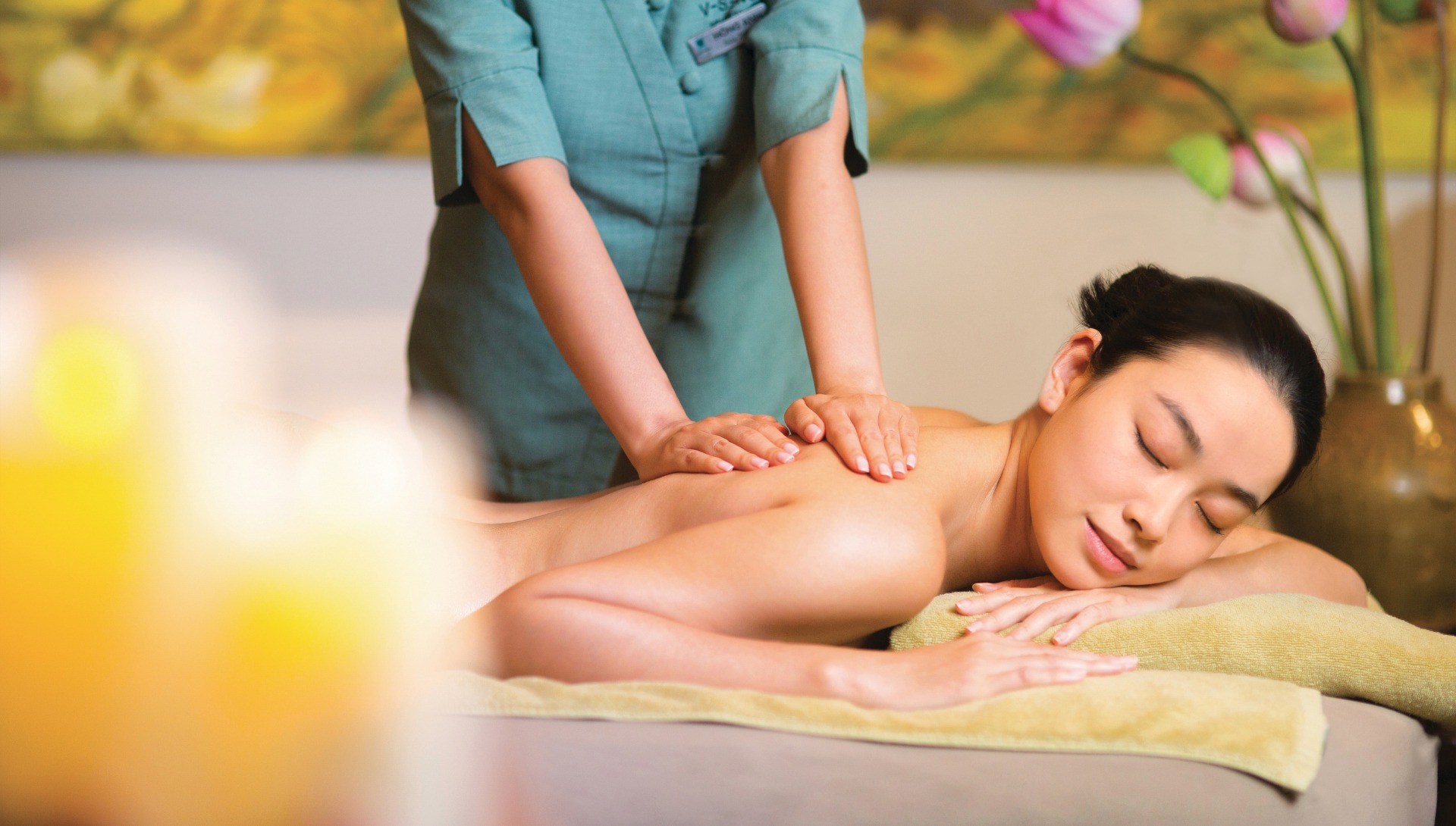 Một kỹ thuật viên chuyên nghiệp trong bộ đồng phục màu xanh mòng két đang massage lưng cho một người phụ nữ thanh thản đang nhắm mắt trên giường trị liệu tại V-Senses Wellness & Spa.