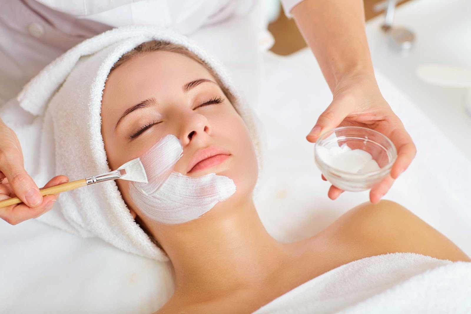 A therapist gently applies a white facial cream mask using a brush onto a woman's cheek during a Marine Anti-Aging treatment at V-Senses Wellness & Spa.