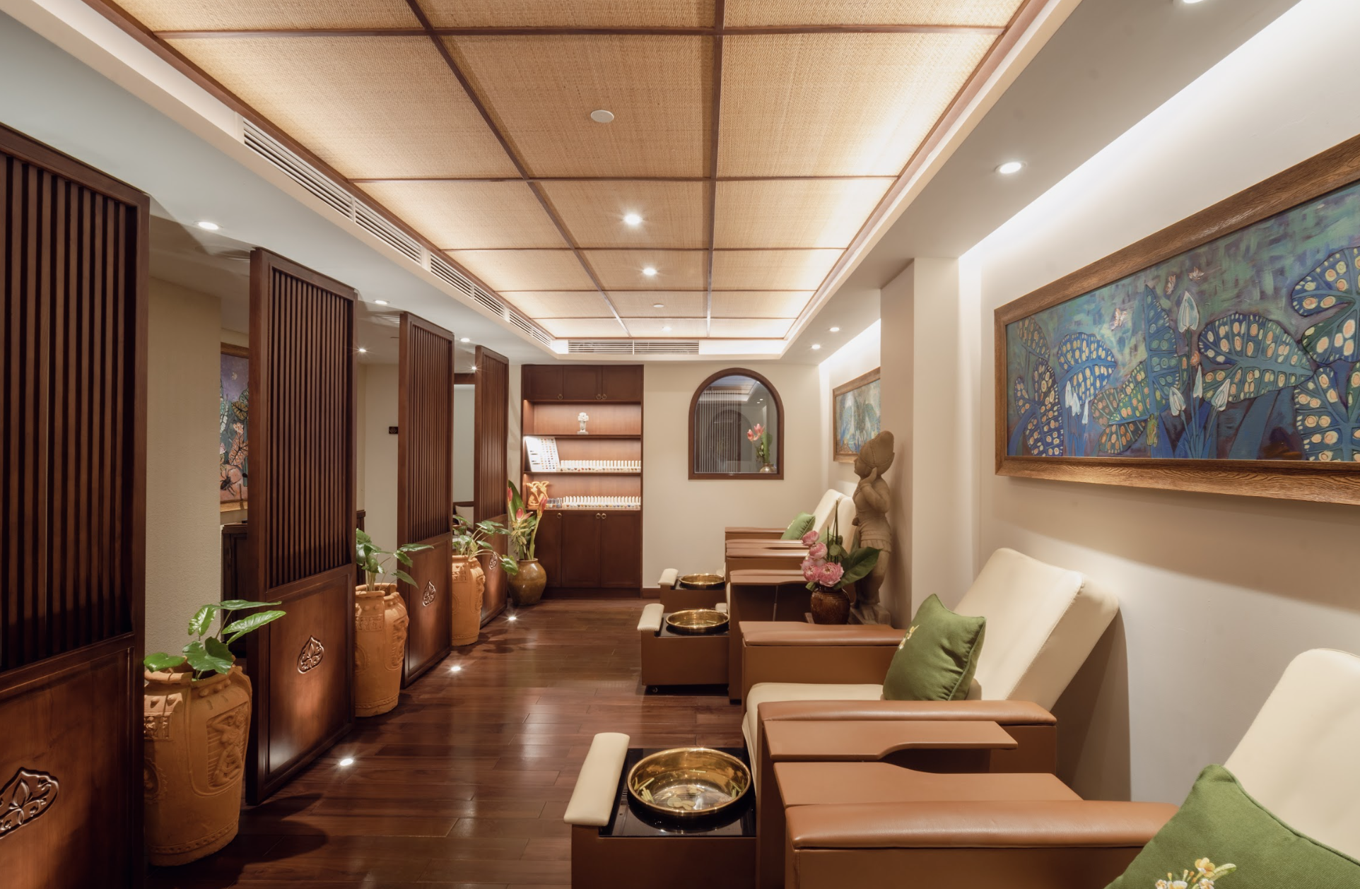 Inside a premium foot reflexology and treatment room at V-Senses Wellness & Spa, featuring elegant leather lounge chairs with green pillows, golden brass foot basins, polished wooden flooring, and traditional wooden partitions.